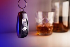 A key fob for a car next to glasses of alcohol with a purple and white background.