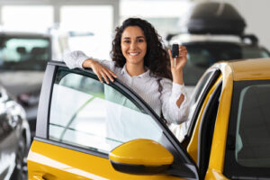 A woman in a white shirt leasing a yellow vehicle at a dealership.