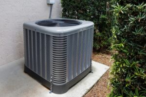 An outdoor air conditioning unit hidden behind hedges on a concrete slab behind a home.