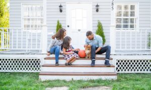 Family sitting on front porch steps with a small dog